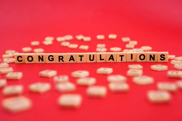 The word CONGRATULATIONS with wooden letter tiles isolated on red background