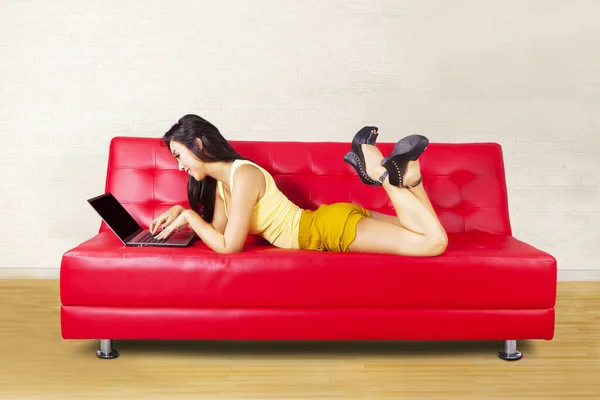 漂亮的亚洲女人享受休闲时间 而躺在桌子上 浏览互联网与笔记本电脑 图库图片