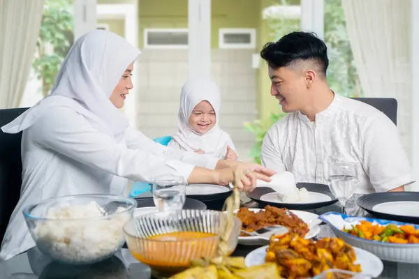若いイスラム教徒のアジア人女性の肖像画は 自宅で娘と微笑んでいる間に夫に食事を与えます ストック写真