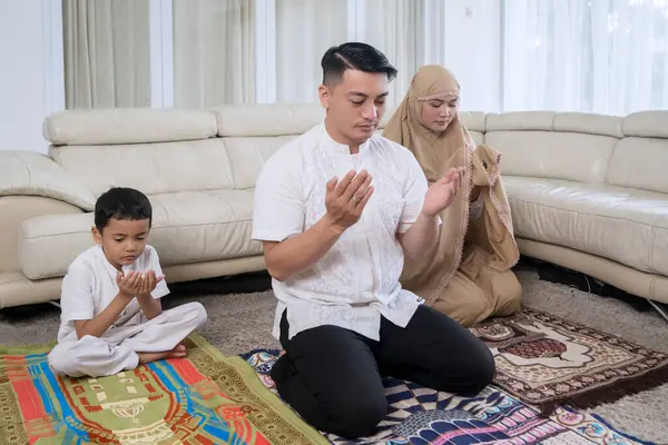 自宅のリビングルームで一緒に祈る若いイスラム教徒の家族 ストックフォト