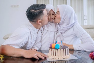 Muslim Parents Kissing Their Daughter on Birthday Celebration at Home clipart