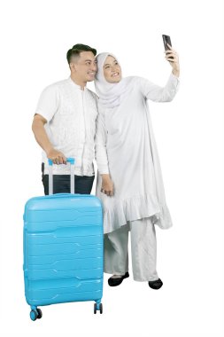 Mutlu Müslüman çift bavulla seyahat ederken selfie çekiyor.