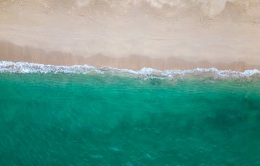 Hava aracı (yukarıdan aşağıya) deniz dalgaları ve beyaz kuma bakıyor. Turkuaz mavi su, tropikal tema. Saf doğada rahatlama kavramı.