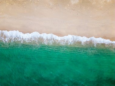 Hava aracı (yukarıdan aşağıya) deniz dalgaları ve beyaz kuma bakıyor. Turkuaz mavi su, tropikal tema. Saf doğada rahatlama kavramı.