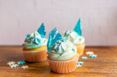 Ahşap masaya konulmuş ev yapımı mavi renkli kek. Kış ve Noel teması, kremalı kar taneleri ve mavi buz. Taze ve ev yapımı tatlı.