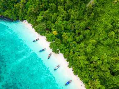 Tayland 'ın Ko Phi adasındaki ünlü Maymun Sahili' nin insansız hava aracı görüntüsü. Beyaz kumu, turkuaz suyu ve yeşil ormanı olan tropik bir sahil. Uzun kuyruklu tekneler sahilde bekliyor. Egzotik turizm merkezi, cennet.