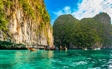 Tayland 'daki Ko Phi Adaları yakınlarındaki okyanusta turkuaz su üzerinde uzun kuyruklu teknelerin görüntüsü. Tropik cennette egzotik tatil kavramı. Arka planda kireçtaşı kayası.