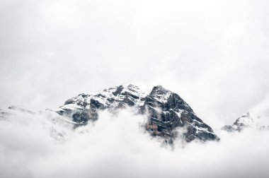 Dolomite tepelerinin yumuşak beyaz bir bulutla örtülü detaylı bir görüntüsü. Dağların engebeli, pürüzlü köşeleri narin sisle tezat oluşturarak dramatik bir doğal manzara yaratıyor.