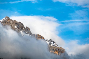Dolomite tepelerinin yumuşak beyaz bir bulutla örtülü detaylı bir görüntüsü. Dağların engebeli, pürüzlü köşeleri narin sisle tezat oluşturarak dramatik bir doğal manzara yaratıyor.