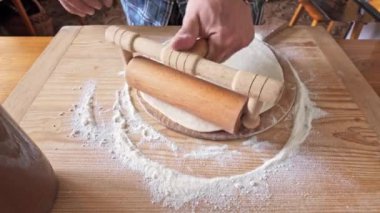 Erkeklerin geleneksel tatlı çörekler için hamuru tahta bir tahtanın üzerinde hazırlarken çekilmiş yakın çekim videosu. Görüntülerde hamuru elle şekillendirdiği, ahşap bir oklava ile yuvarladığı, ve sonunda onu erik reçeli ile doldurduğu, zanaat sürecini yakaladığı görülüyor.
