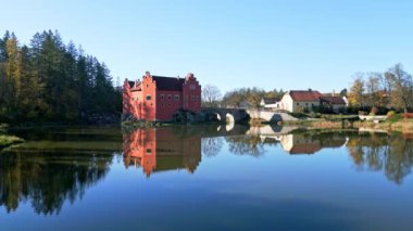 Cervena Lhota Kalesi 'nin (Red Chateau, Schloss Rot) panoramik drone görüntüsü, aşağıdaki göletteki kalelerin yansımasını gösterir. Sonbahar renkli ormanlarla çevrili