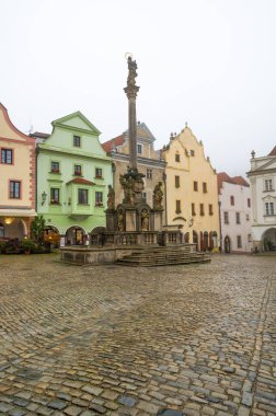 Cesky Krumlov 'daki karenin kasvetli sonbahar manzarası, Barok Veba Sütunu' nu içeren Bakire Meryem Immaculata heykeli, sis, yağmur ve sakin bir atmosferle çevrili.