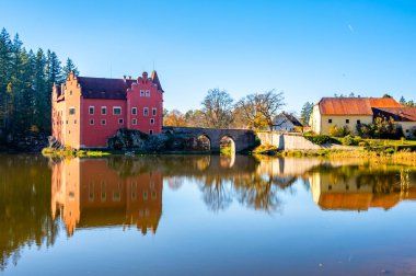 Çek Cumhuriyeti 'ndeki Cervena Lhota Kalesi' nin panoramik manzarası, görüntüsünü yansıtan bir gölle çevrili. Parlak renkte sonbahar ağaçları ve güneşli hava resim gibi, sakin bir manzara yaratır..