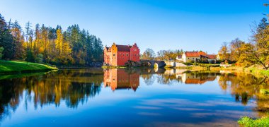 Çek Cumhuriyeti 'ndeki Cervena Lhota Kalesi' nin panoramik manzarası, görüntüsünü yansıtan bir gölle çevrili. Parlak renkte sonbahar ağaçları ve güneşli hava resim gibi, sakin bir manzara yaratır..