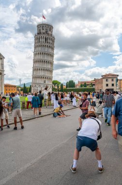 Pisa, İtalya - 12.6.2024: Eğik Pisa Kulesi önünde poz veren turistler (Torre Pendente di Pisa), simgesel eğimli yapıyı destekliyormuş gibi görünmek için zorla perspektif kullanıyorlar.