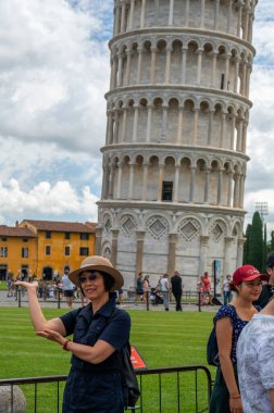 Pisa, İtalya - 12.6.2024: Eğik Pisa Kulesi önünde poz veren turistler (Torre Pendente di Pisa), simgesel eğimli yapıyı destekliyormuş gibi görünmek için zorla perspektif kullanıyorlar.