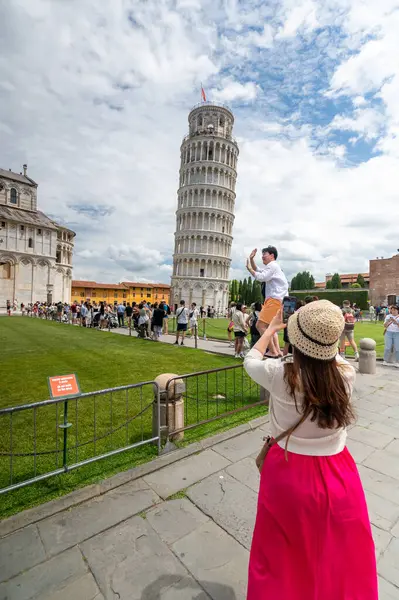 Pisa, İtalya - 12.6.2024: Eğik Pisa Kulesi önünde poz veren turistler (Torre Pendente di Pisa), simgesel eğimli yapıyı destekliyormuş gibi görünmek için zorla perspektif kullanıyorlar.