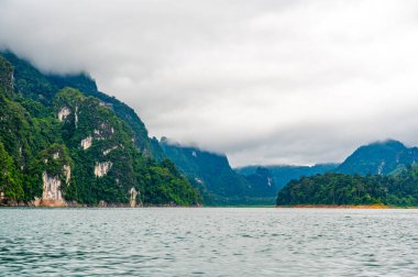 Tayland 'ın Krabi ilindeki Khao Sok Gölü manzarası. Yüksek kireçtaşı uçurumları, gölün sakin yüzeyinden yükselen tropikal yağmur ormanlarıyla kaplı..
