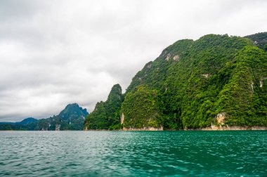 Tayland 'ın Krabi ilindeki Khao Sok Gölü manzarası. Yüksek kireçtaşı uçurumları, gölün sakin yüzeyinden yükselen tropikal yağmur ormanlarıyla kaplı..