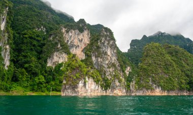 Tayland 'ın Krabi ilindeki Khao Sok Gölü manzarası. Yüksek kireçtaşı uçurumları, gölün sakin yüzeyinden yükselen tropikal yağmur ormanlarıyla kaplı..