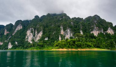 Tayland 'ın Krabi ilindeki Khao Sok Gölü manzarası. Yüksek kireçtaşı uçurumları, gölün sakin yüzeyinden yükselen tropikal yağmur ormanlarıyla kaplı..