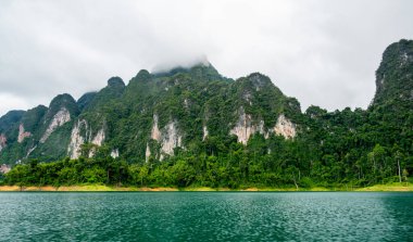 Tayland 'ın Krabi ilindeki Khao Sok Gölü manzarası. Yüksek kireçtaşı uçurumları, gölün sakin yüzeyinden yükselen tropikal yağmur ormanlarıyla kaplı..