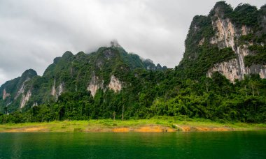 Tayland 'ın Krabi ilindeki Khao Sok Gölü manzarası. Yüksek kireçtaşı uçurumları, gölün sakin yüzeyinden yükselen tropikal yağmur ormanlarıyla kaplı..