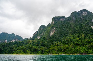 Tayland 'ın Krabi ilindeki Khao Sok Gölü manzarası. Yüksek kireçtaşı uçurumları, gölün sakin yüzeyinden yükselen tropikal yağmur ormanlarıyla kaplı..