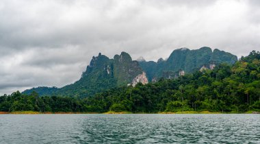Tayland 'ın Krabi ilindeki Khao Sok Gölü manzarası. Yüksek kireçtaşı uçurumları, gölün sakin yüzeyinden yükselen tropikal yağmur ormanlarıyla kaplı..