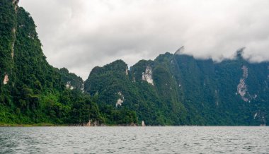 Tayland 'ın Krabi ilindeki Khao Sok Gölü manzarası. Yüksek kireçtaşı uçurumları, gölün sakin yüzeyinden yükselen tropikal yağmur ormanlarıyla kaplı..