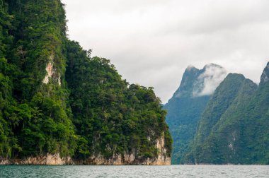 Tayland 'ın Krabi ilindeki Khao Sok Gölü manzarası. Yüksek kireçtaşı uçurumları, gölün sakin yüzeyinden yükselen tropikal yağmur ormanlarıyla kaplı..