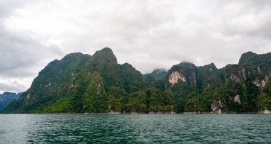 Tayland 'ın Krabi ilindeki Khao Sok Gölü manzarası. Yüksek kireçtaşı uçurumları, gölün sakin yüzeyinden yükselen tropikal yağmur ormanlarıyla kaplı..