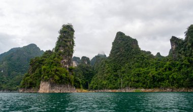 Tayland 'ın Krabi ilindeki Khao Sok Gölü manzarası. Yüksek kireçtaşı uçurumları, gölün sakin yüzeyinden yükselen tropikal yağmur ormanlarıyla kaplı..