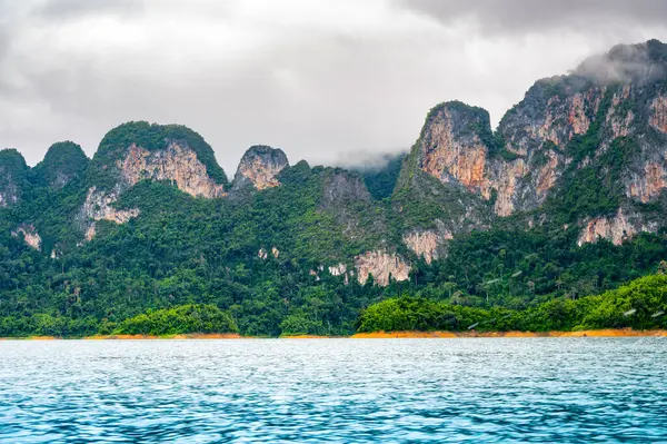 Tayland 'ın Krabi ilindeki Khao Sok Gölü manzarası. Yüksek kireçtaşı uçurumları, gölün sakin yüzeyinden yükselen tropikal yağmur ormanlarıyla kaplı..