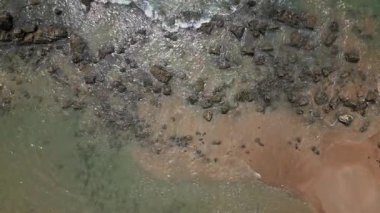 Sahildeki kum ve siyah kayaların üzerinden geçen dalgaların yukarıdan aşağıya havadan görünüşü soyut su, taş ve kıyı şeritlerini oluşturan küçük bir koy oluşturur..