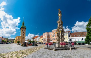 Avusturya, Retz 'deki ana meydanın panoramik manzarası, Kutsal Üçlü Sütun, renkli binalar, belediye kulesi, çiçek açan çiçekler ve sıcak yaz atmosferi.