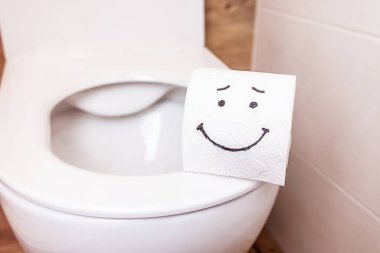 Tuvalet kağıdı rulosunun yakın çekimi ve banyo duvarında komik bir emoji asılı. Sağlık konsepti, temiz banyo, mutlu hayat. Dizaynınız ve metniniz için yapıştır
