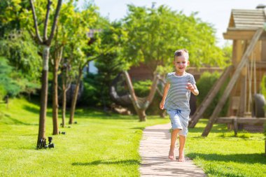 Küçük bir çocuk yaz bahçesinde oynuyor. Güneşli bir yaz gününde bir çocuk patika boyunca koşar. Yaz tatili konsepti, mutlu tasasız çocukluk. Aile kavramı. kopyala yapıştır