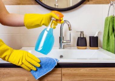 Beyaz şişe tutan koruyucu eldivenli bir kadın elinin yakın çekimi, temizlik ajanı modeli, logo ve etiket için yer. Banyo arkaplanı. Hijyen, temizlik ve temizlik kavramı.