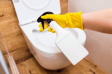 Tuvalet temizleyicili plastik beyaz bir şişe, logo için yer. Temizlik, dezenfeksiyon ve tuvalet temizliği için temizleme solüsyonu ve paçavralar kullanan koruyucu eldivenlerle kadın ellerine yakın çekim