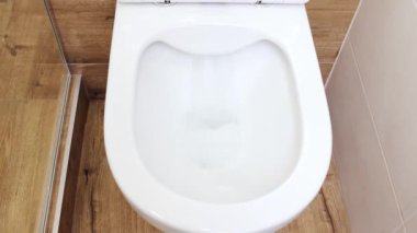 Sifonu çekilen beyaz bir tuvaletin yakın görüntüsü. Su klozetin içinde döner. Beyaz tuvalet fırçası klozeti temizlemeye hazır, ev temizliği konsepti ve ev işleri.