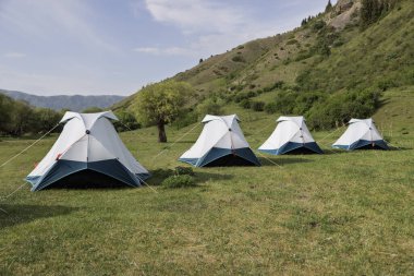 Kazakistan dağlarına kurulmuş gri kamp çadırları, göz kamaştırıcı doğal manzaralarla çevrili.
