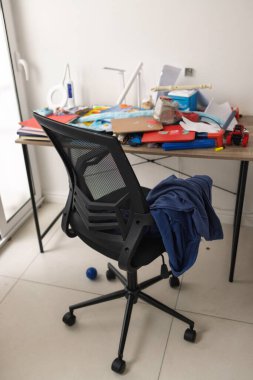 Okul kitapları, sırt çantası ve dağınık malzemelerle dolu dağınık bir çalışma alanı. Gençlik alışkanlıklarını sembolize ediyor