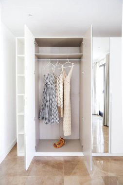 Açık gardırop, üç asılı elbise ve parlak şık odada yerde bir çift ayakkabı..