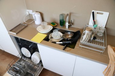 Kirli bulaşıklar lavaboda ve bulaşık makinesinde çatal bıçak, tabak, sünger ve sabun var..