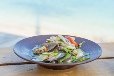 Baharatlı deniz ürünleri salatası, ahşap bir masada popüler yemek, denizin yanındaki bir kafede iştah açıcı, Sue Flamingo, Ao Yon Sahili, Phuket Tayland