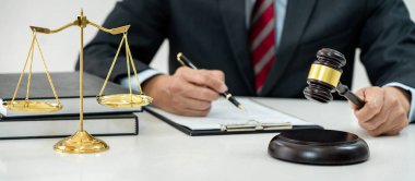 Sözleşme kağıtları, kitap ve ahşap tokmakla çalışan bir erkek avukat veya noter mahkeme salonunda, hukuk ve hukuk hizmetleri kavramında masaya oturur..