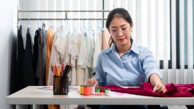 Kadın moda tasarımcısı çalışıyor ve kumaş malzemelerini ölçüyor. Yeni kıyafet koleksiyonu ürünleri yapmak için renk örnekleri seçiyor..