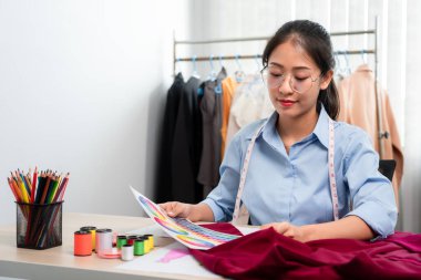 Kadın moda tasarımcısı çalışıyor ve kumaş malzemelerini ölçüyor. Yeni kıyafet koleksiyonu ürünleri yapmak için renk örnekleri seçiyor..