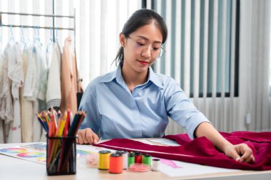 Kadın moda tasarımcısı çalışıyor ve kumaş malzemelerini ölçüyor. Yeni kıyafet koleksiyonu ürünleri yapmak için renk örnekleri seçiyor..